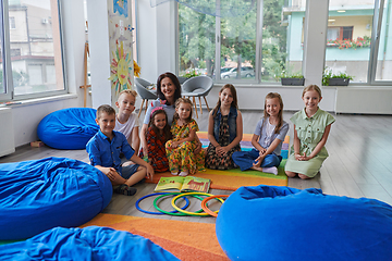 Image showing A happy female teacher sitting and playing hand games with a group of little schoolchildren