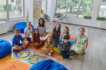 Image showing A happy female teacher sitting and playing hand games with a group of little schoolchildren