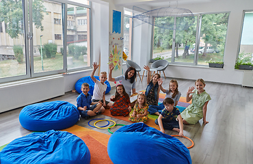 Image showing A happy female teacher sitting and playing hand games with a group of little schoolchildren