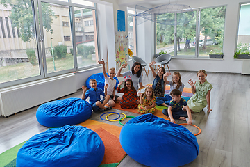 Image showing A happy female teacher sitting and playing hand games with a group of little schoolchildren