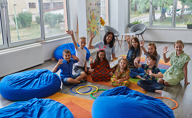 Image showing A happy female teacher sitting and playing hand games with a group of little schoolchildren