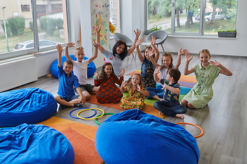 Image showing A happy female teacher sitting and playing hand games with a group of little schoolchildren