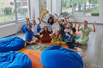 Image showing A happy female teacher sitting and playing hand games with a group of little schoolchildren