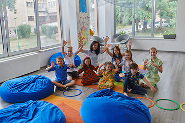 Image showing A happy female teacher sitting and playing hand games with a group of little schoolchildren