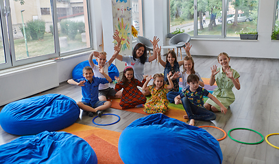 Image showing A happy female teacher sitting and playing hand games with a group of little schoolchildren