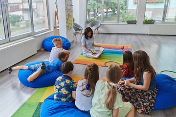 Image showing Reading time in an elementary school or kindergarten, a teacher reading a book to children in an elementary school or kindergarten. The concept of pre-school education. Selective focus