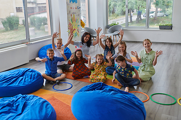 Image showing A happy female teacher sitting and playing hand games with a group of little schoolchildren