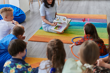 Image showing Reading time in an elementary school or kindergarten, a teacher reading a book to children in an elementary school or kindergarten. The concept of pre-school education. Selective focus