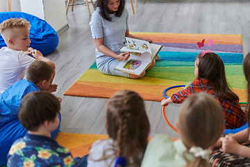 Image showing Reading time in an elementary school or kindergarten, a teacher reading a book to children in an elementary school or kindergarten. The concept of pre-school education. Selective focus