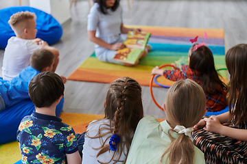 Image showing Reading time in an elementary school or kindergarten, a teacher reading a book to children in an elementary school or kindergarten. The concept of pre-school education. Selective focus