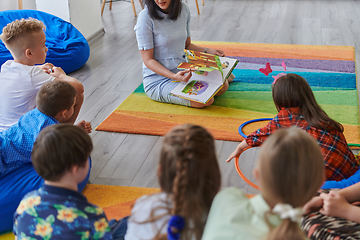 Image showing Reading time in an elementary school or kindergarten, a teacher reading a book to children in an elementary school or kindergarten. The concept of pre-school education. Selective focus