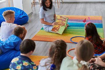 Image showing Reading time in an elementary school or kindergarten, a teacher reading a book to children in an elementary school or kindergarten. The concept of pre-school education. Selective focus