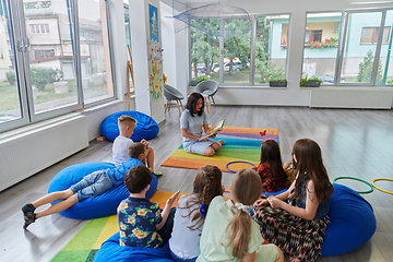 Image showing Reading time in an elementary school or kindergarten, a teacher reading a book to children in an elementary school or kindergarten. The concept of pre-school education. Selective focus