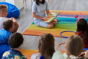 Image showing Reading time in an elementary school or kindergarten, a teacher reading a book to children in an elementary school or kindergarten. The concept of pre-school education. Selective focus