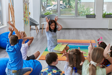 Image showing A happy female teacher sitting and playing hand games with a group of little schoolchildren