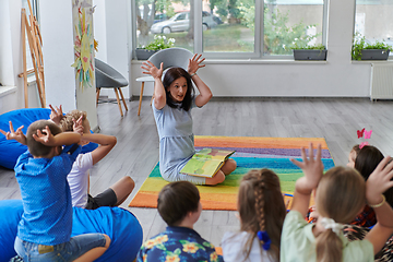 Image showing A happy female teacher sitting and playing hand games with a group of little schoolchildren