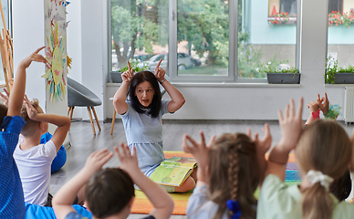 Image showing A happy female teacher sitting and playing hand games with a group of little schoolchildren