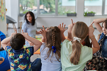 Image showing A happy female teacher sitting and playing hand games with a group of little schoolchildren