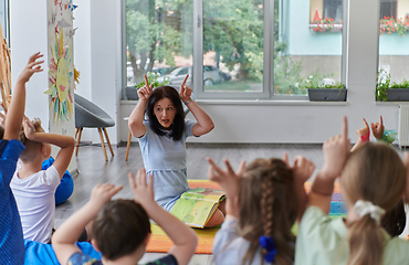 Image showing A happy female teacher sitting and playing hand games with a group of little schoolchildren