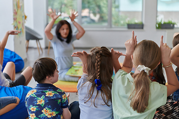 Image showing A happy female teacher sitting and playing hand games with a group of little schoolchildren