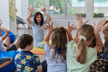 Image showing A happy female teacher sitting and playing hand games with a group of little schoolchildren