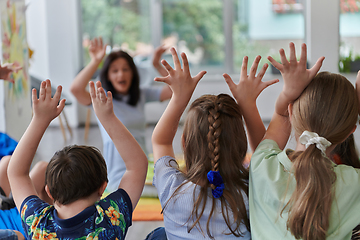 Image showing A happy female teacher sitting and playing hand games with a group of little schoolchildren