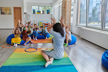 Image showing A happy female teacher sitting and playing hand games with a group of little schoolchildren