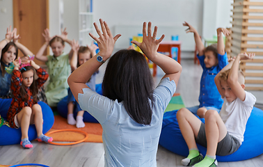 Image showing A happy female teacher sitting and playing hand games with a group of little schoolchildren