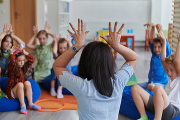 Image showing A happy female teacher sitting and playing hand games with a group of little schoolchildren