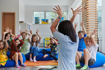 Image showing A happy female teacher sitting and playing hand games with a group of little schoolchildren