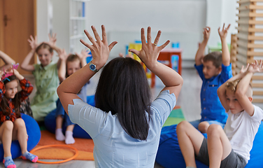 Image showing A happy female teacher sitting and playing hand games with a group of little schoolchildren