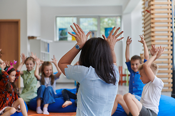 Image showing A happy female teacher sitting and playing hand games with a group of little schoolchildren