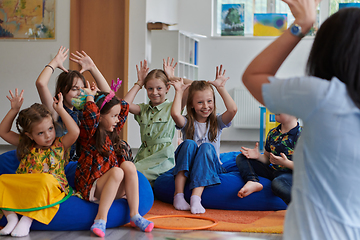 Image showing A happy female teacher sitting and playing hand games with a group of little schoolchildren