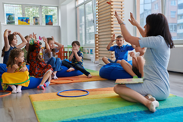 Image showing A happy female teacher sitting and playing hand games with a group of little schoolchildren