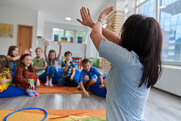 Image showing A happy female teacher sitting and playing hand games with a group of little schoolchildren