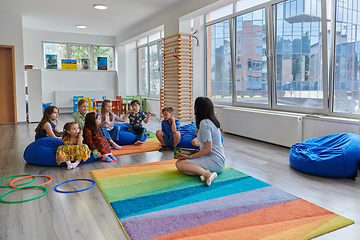 Image showing Reading time in an elementary school or kindergarten, a teacher reads a book to children in an elementary school or kindergarten. The concept of pre-school education. Selective focus