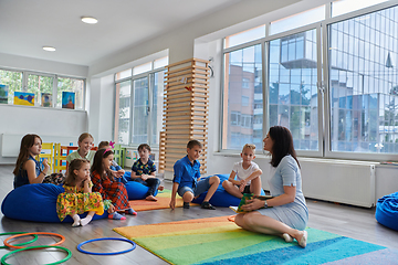 Image showing Reading time in an elementary school or kindergarten, a teacher reads a book to children in an elementary school or kindergarten. The concept of pre-school education. Selective focus