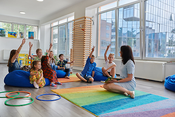 Image showing Reading time in an elementary school or kindergarten, a teacher reads a book to children in an elementary school or kindergarten. The concept of pre-school education. Selective focus