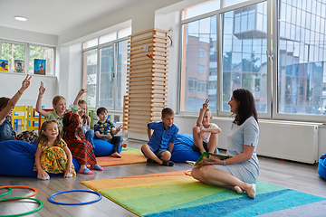 Image showing Reading time in an elementary school or kindergarten, a teacher reads a book to children in an elementary school or kindergarten. The concept of pre-school education. Selective focus