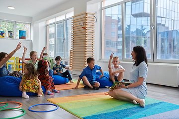 Image showing Reading time in an elementary school or kindergarten, a teacher reads a book to children in an elementary school or kindergarten. The concept of pre-school education. Selective focus