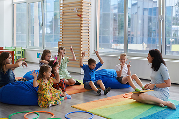 Image showing Reading time in an elementary school or kindergarten, a teacher reads a book to children in an elementary school or kindergarten. The concept of pre-school education. Selective focus