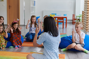 Image showing A happy female teacher sitting and playing hand games with a group of little schoolchildren