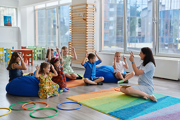 Image showing Reading time in an elementary school or kindergarten, a teacher reads a book to children in an elementary school or kindergarten. The concept of pre-school education. Selective focus