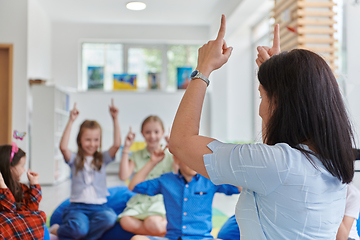 Image showing A happy female teacher sitting and playing hand games with a group of little schoolchildren