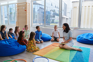 Image showing Reading time in an elementary school or kindergarten, a teacher reads a book to children in an elementary school or kindergarten. The concept of pre-school education. Selective focus