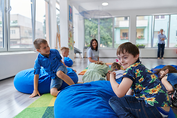 Image showing A happy female teacher sitting and playing hand games with a group of little schoolchildren