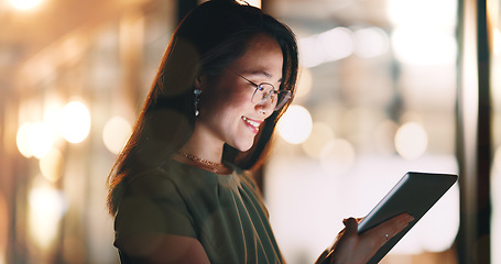 Image showing Asian woman, tablet and typing in night office while working on project deadline. Digital tech, touchscreen and happy business woman working late in dark workplace, researching and writing email.