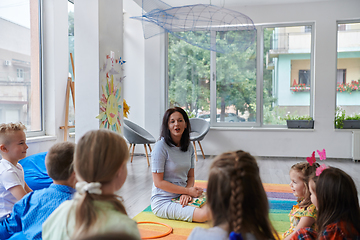 Image showing A happy female teacher sitting and playing hand games with a group of little schoolchildren