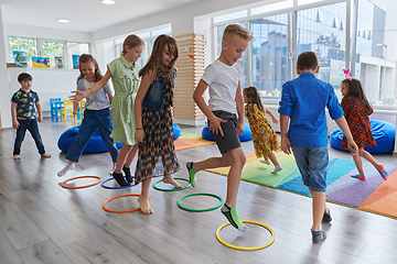 Image showing Small nursery school children with female teacher on floor indoors in classroom, doing exercise. Jumping over hula hoop circles track on the floor.