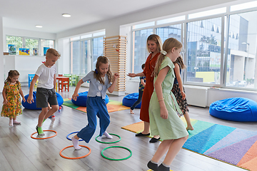 Image showing Small nursery school children with female teacher on floor indoors in classroom, doing exercise. Jumping over hula hoop circles track on the floor.